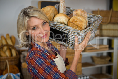 Portrait of smiling female staff carrying wicker basket of various breads at counter