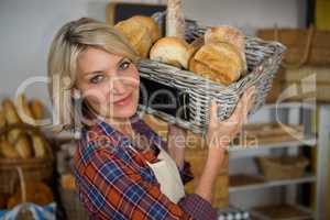 Portrait of smiling female staff carrying wicker basket of various breads at counter