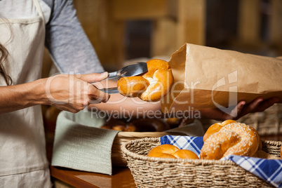 Staff packing bread in paper bag at bakery shop