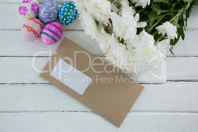 Multicolored Easter eggs, bunch of flower and envelope on wooden background