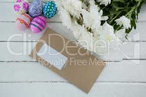 Multicolored Easter eggs, bunch of flower and envelope on wooden background