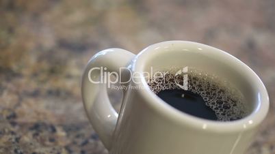 Pouring Coffee Creamer Into Coffee Mug on Granite Counter Top in Kitchen.