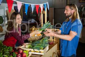 Smiling female staff offering vegetables to customer at organic section