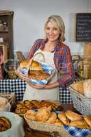 Smiling female staff holding wicker basket of breads at counter