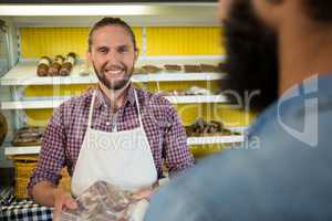 Portrait of smiling male staff holding a meat packet at counter