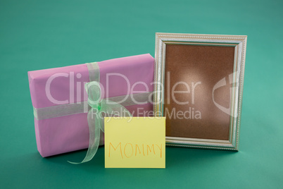 Gift box, photo frame with text mom on card against green background