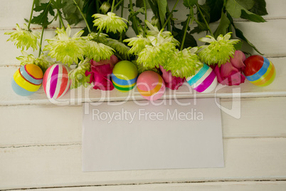 Painted Easter eggs, bunch of flower and envelope on wooden background