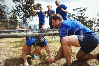 Fit woman crawling under the net during obstacle course while fit people cheering