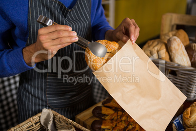 Mid section of staff packing croissant in paper bag at counter