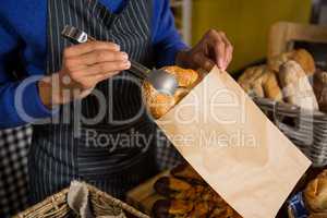 Mid section of staff packing croissant in paper bag at counter
