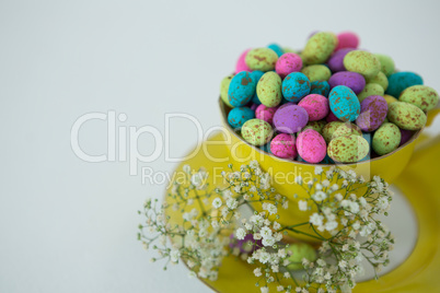 Cup filled with colorful chocolate Easter eggs and white flower