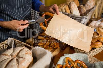 Mid section of staff packing pretzel bread in paper bag at counter