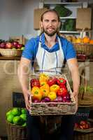 Smiling male staff standing with basket of bell peppers at organic section