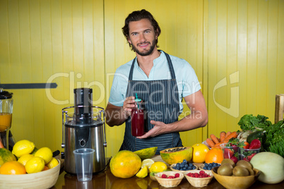 Portrait of smiling male staff holding juice bottle at counter