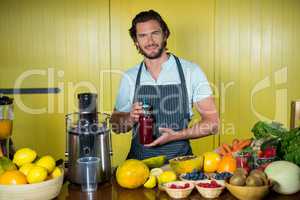 Portrait of smiling male staff holding juice bottle at counter