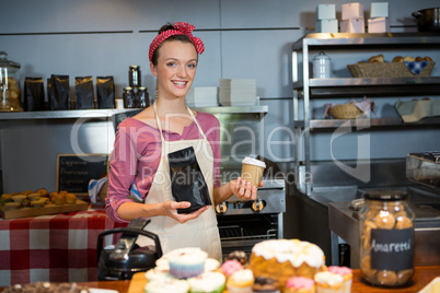 Portrait of female staff holding coffee bag and coffee cup at counter