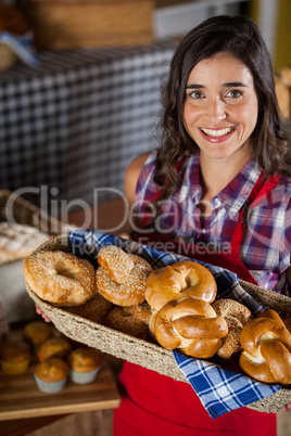 Smiling female staff holding wicker basket of various breads at counter