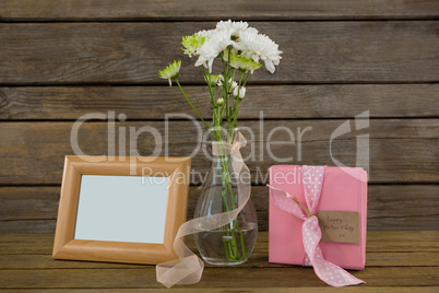 Gift box, photo frame and flower vase on wooden surface