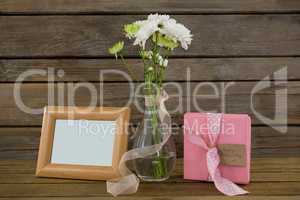 Gift box, photo frame and flower vase on wooden surface