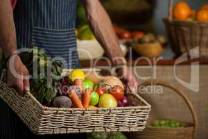 Mid section of male staff holding fresh vegetables in basket at organic section