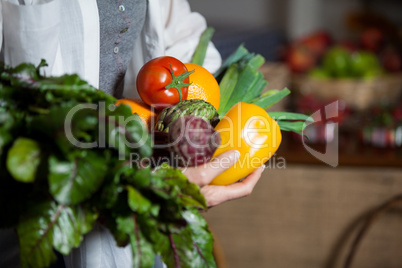 Mid section female costumer holding fresh vegetables and fruits in organic section