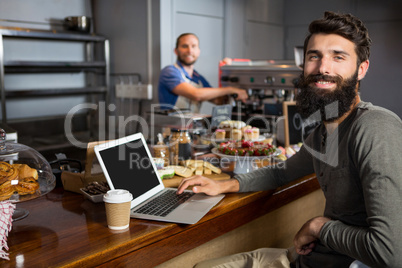 Male customer using laptop while having coffee at counter in coffee shop