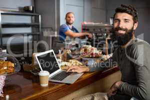Male customer using laptop while having coffee at counter in coffee shop