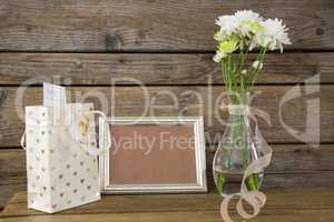 Gift bag, photo frame and flower vase on wooden surface