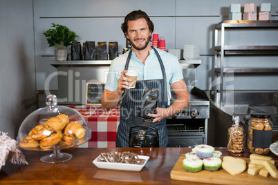 Portrait of male staff holding coffee cup and coffee bag at counter