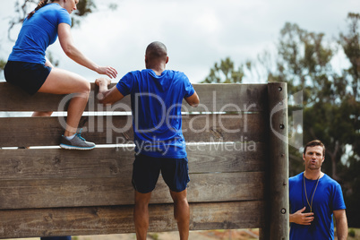 Female trainer assisting man to climb a wooden wall