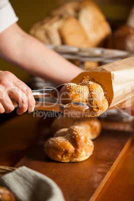 Hands of female staff packing sweet food in paper bag