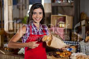 Smiling female staff packing sweet food in paper bag at counter in bakery shop