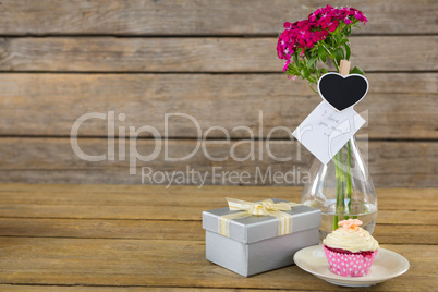 Gift box and flower vase with cupcake in plate on wooden plank