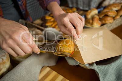 Mid section of staff packing cup cake in paper bag at counter