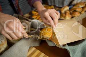 Mid section of staff packing cup cake in paper bag at counter