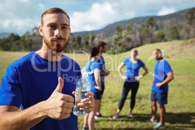 Fit man showing thumbs up while holding water bottle