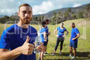 Fit man showing thumbs up while holding water bottle
