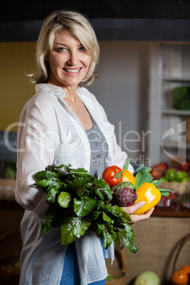 Portrait female costumer holding fresh vegetables and fruits in organic section