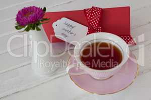 Black tea, flower vase and happy mothers day card on wooden surface