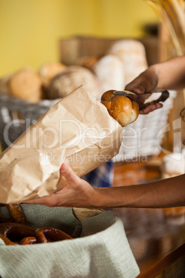 Staff packing bread in paper bag at bakery shop