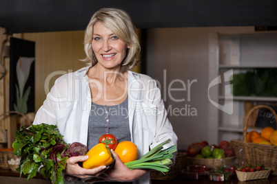 Portrait female costumer holding fresh vegetables and fruits in organic section