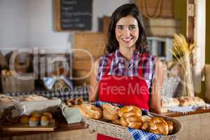 Smiling female staff holding wicker basket of various breads at counter