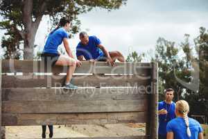 Female trainer assisting man to climb a wooden wall