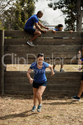 Woman running while trainer assisting men to climb a wooden wall