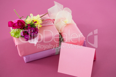 Gift boxes with flowers and blank card against pink background