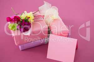 Gift boxes with flowers and blank card against pink background