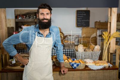 Portrait of smiling male staff standing with hands on hip at counter