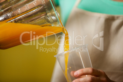 Female staff pouring juice into glass at counter