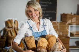 Female staff holding basket of bread in bakery section