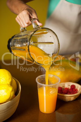 Female staff pouring juice into glass at counter